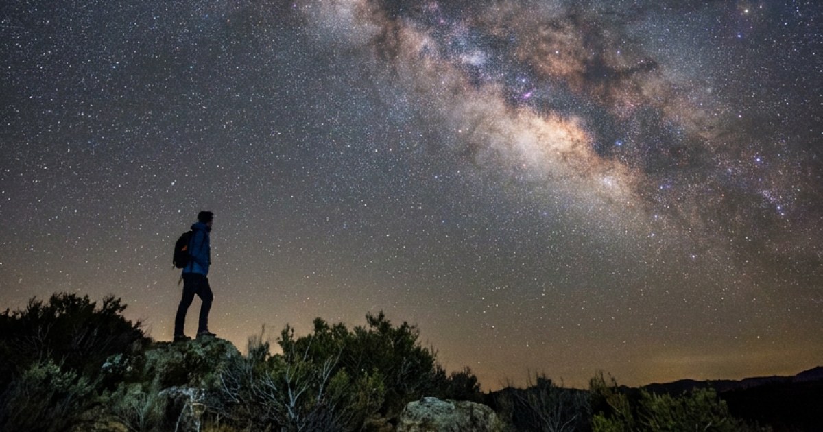 A photorealistic man standing beneath an enormous night sky filled wit